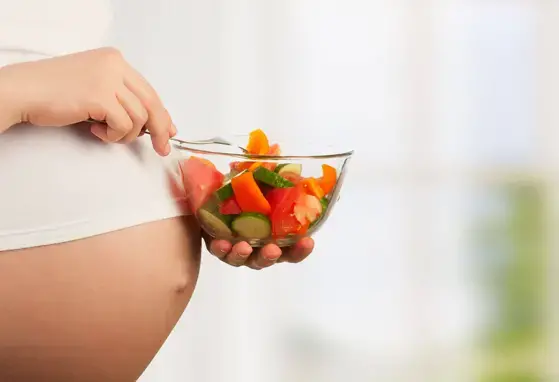Una alimentación balanceada es fundamental durante el embarazo. Mujer embarazada con un plato de verduras para hacer ensaladas.