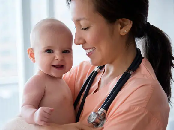 Una doctora sostiene en sus brazos a un bebé.